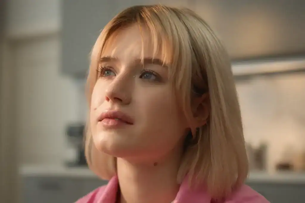 Trauma Solutions: A young person with short blonde hair and blue eyes looks slightly upward, wearing a pink shirt, radiating self-esteem against a soft indoor background. Thoughtful young woman representing the emotional experience of addiction, attachment wounds, and the search for connection.