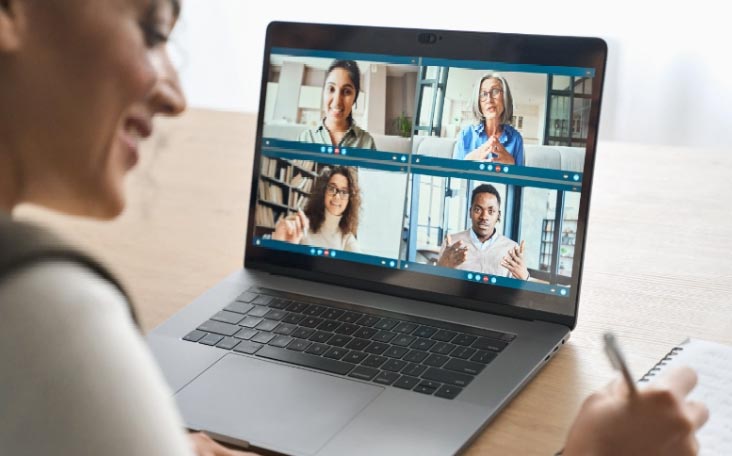 A woman on a laptop participates in a video call with a group of people, discussing the Attachment & Trauma Mastery Program.