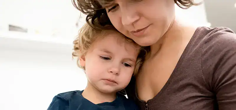 Trauma Solutions: A woman holds a young child who appears sad, resting their head on her chest in a close, comforting embrace.
