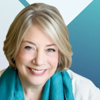 Trauma Solutions: Smiling woman with short gray-blonde hair, wearing a turquoise scarf and white top, posed in front of a blue geometric background.