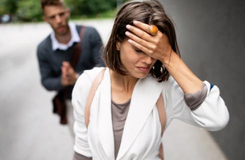 A woman covering her face while a man is walking down the street.