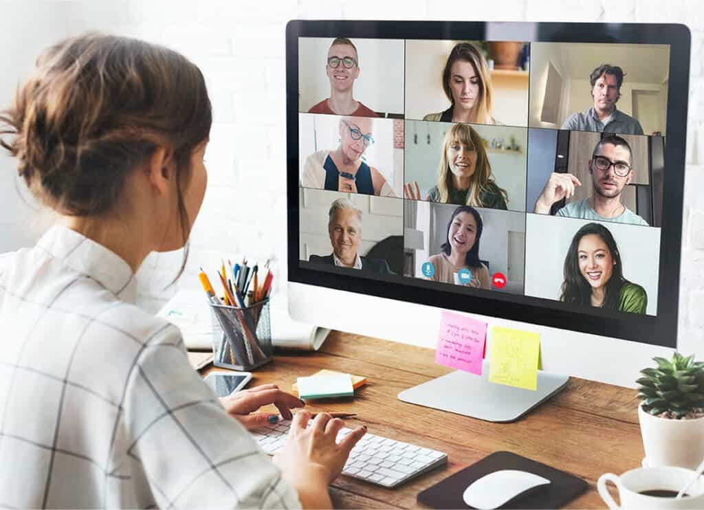 Trauma Solutions: A person sits at a desk using a desktop computer for a video conference with nine people, each visible in separate windows on the monitor.