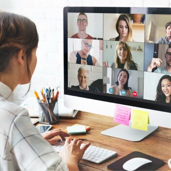 Trauma Solutions: A person sits at a desk using a desktop computer for a video conference with nine people, each visible in separate windows on the monitor.