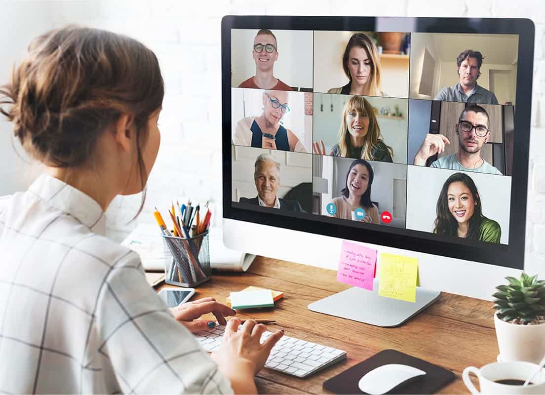 Trauma Solutions: A person sits at a desk using a desktop computer for a video conference with nine people, each visible in separate windows on the monitor.