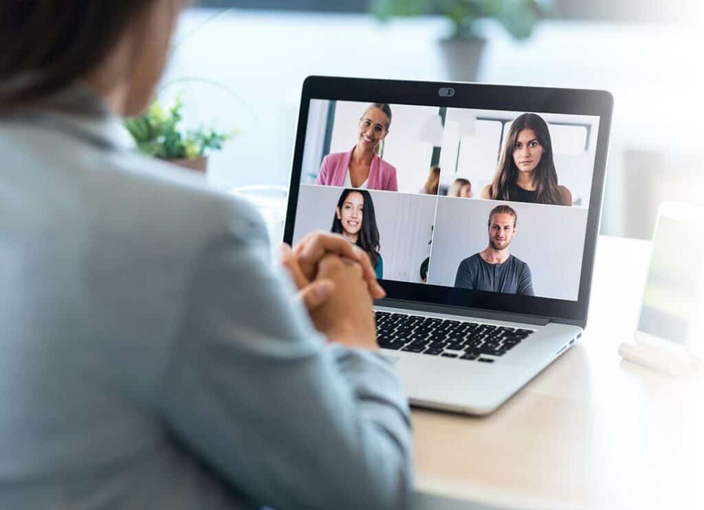 Trauma Solutions: Person sitting at a desk participating in a video call with four other people, all visible on a laptop screen in a grid layout.