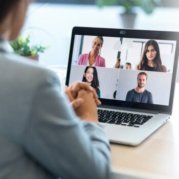Trauma Solutions: Person sitting at a desk participating in a video call with four other people, all visible on a laptop screen in a grid layout.