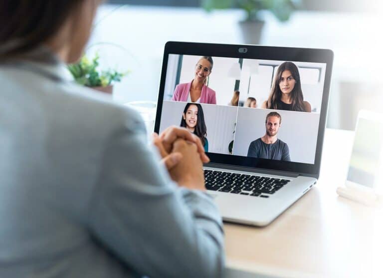 Trauma Solutions: Person sitting at a desk participating in a video call with four other people, all visible on a laptop screen in a grid layout.