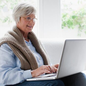 An older woman participating in Case Consult Group Training with Jennifer Jonell while using a laptop.
