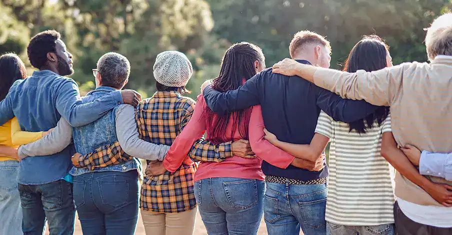 Trauma Solutions: A group of people stand outdoors with their arms around each other’s backs, facing away from the camera.