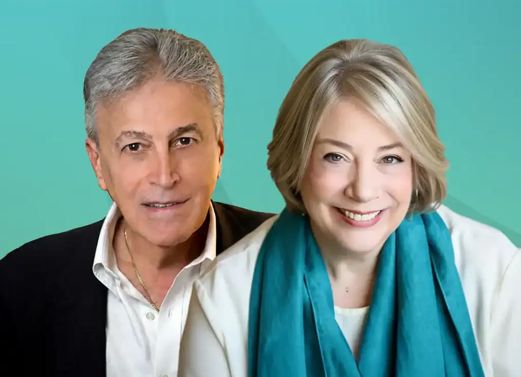 Trauma Solutions: A man and a woman, both with gray hair, are smiling and posing against a teal background. The woman is wearing a teal scarf.