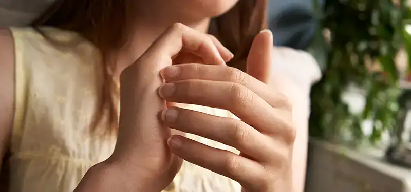 Trauma Solutions: A person in a sleeveless yellow top touches the fingers of their left hand with their right hand, practicing mindfulness; greenery is visible in the background.