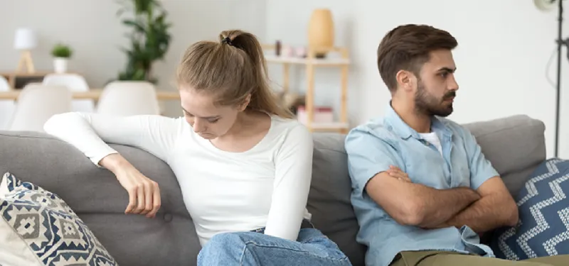 Distant couple sitting back-to-back on a couch, each looking away—illustrating emotional misattunement and the withdrawal-pursuit dynamic in relationships.