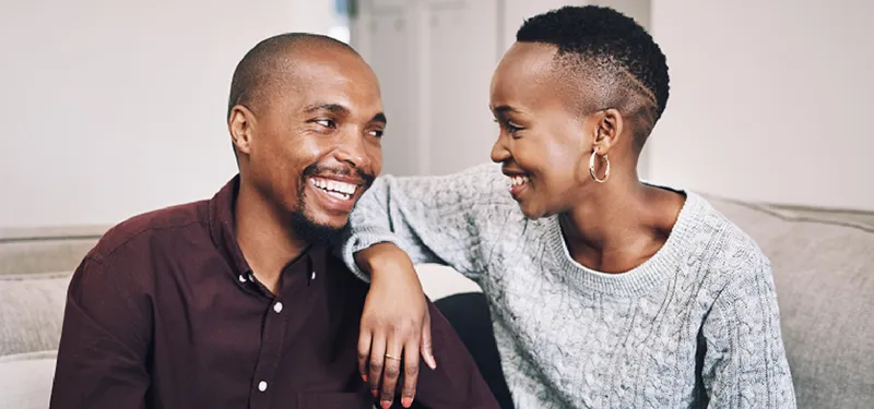 Smiling couple making eye contact on the couch—representing mutual understanding, emotional attunement, and the potential for reconnection after shutdown