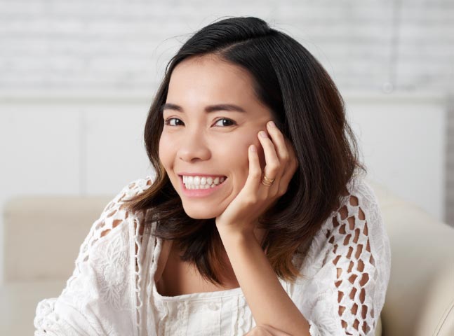 A smiling asian woman sitting on a couch.