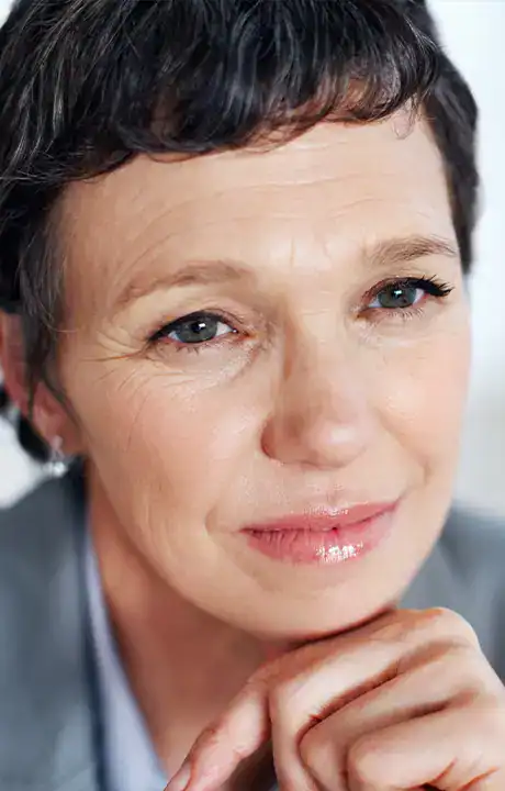 Trauma Solutions: Close-up of an older woman with short dark hair, light eyes, and a thoughtful expression, resting her chin on her hand.