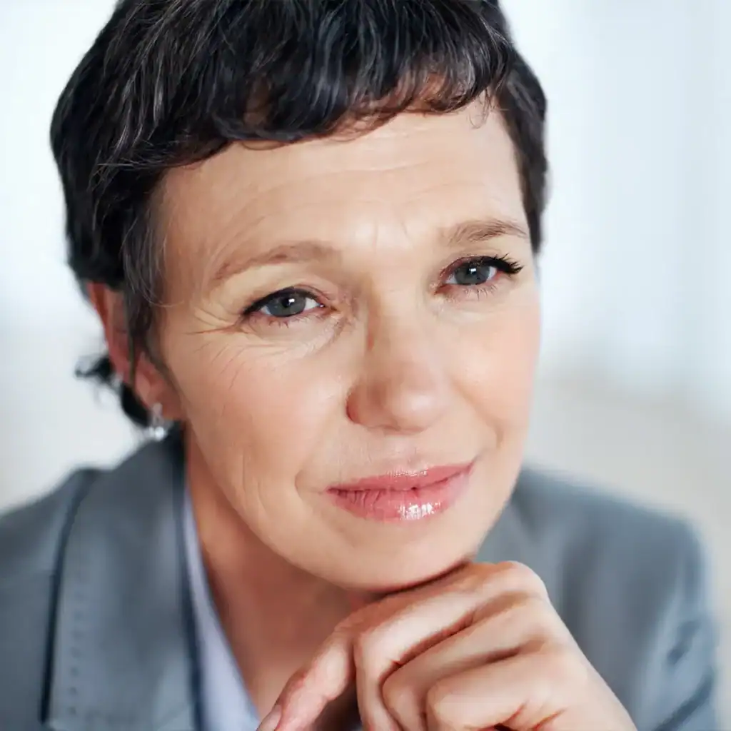 Trauma Solutions: A woman with short dark hair and a gray blazer looks thoughtfully ahead, resting her chin on her hand.