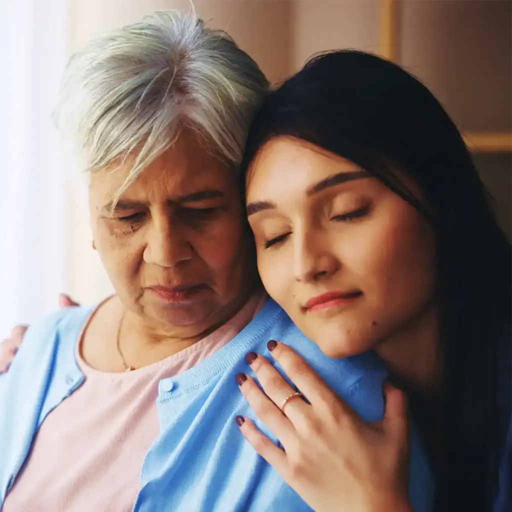 Trauma Solutions: An older woman with gray hair looks down while a younger woman with long dark hair rests her head on the older woman's shoulder, eyes closed.
