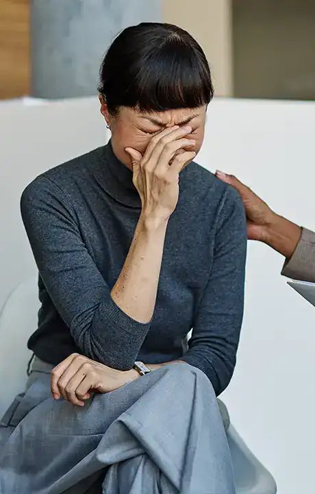 Trauma Solutions: A person sits with eyes closed and hand covering face, while another hand rests on their shoulder, offering comfort.