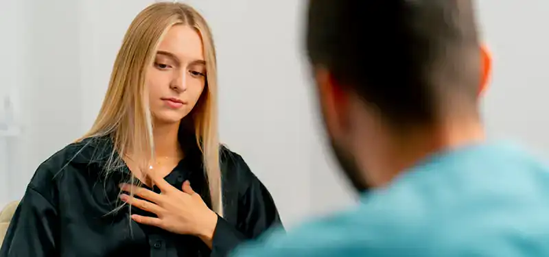 A female client pauses during therapy, her eyes downturned and hand raised to her chest. These subtle somatic cues can signal the presence of shame, before it arises as a thought or emotion.
