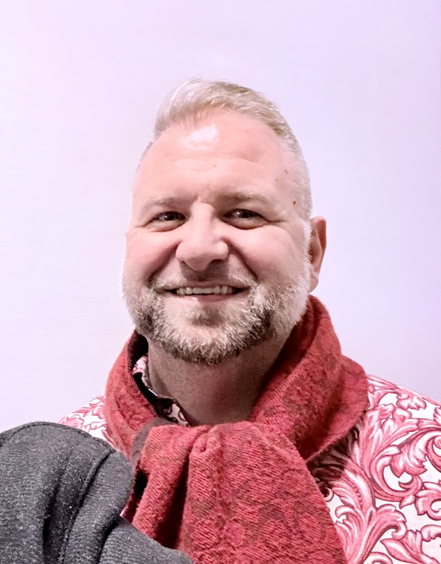 Trauma Solutions: A man with short blond hair and a beard, wearing a red patterned shirt and a red scarf, smiling in front of a plain light background.