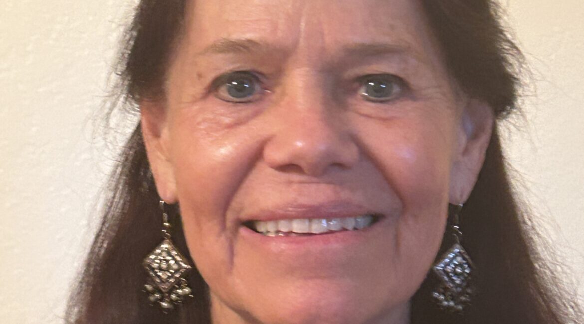 Trauma Solutions: A woman with long brown hair, wearing a red top and dangling earrings, smiles at the camera against a plain light-colored background.