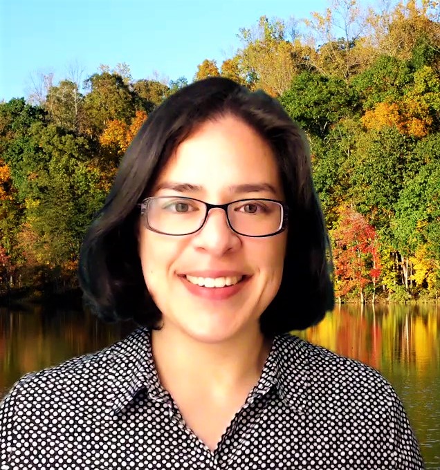 Trauma Solutions: A person with dark hair and glasses smiles in front of a background of autumn trees and a lake.