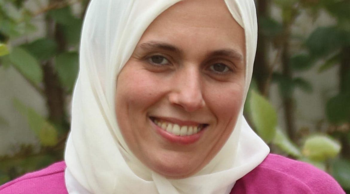 A woman wearing a white hijab smiles for the camera.
