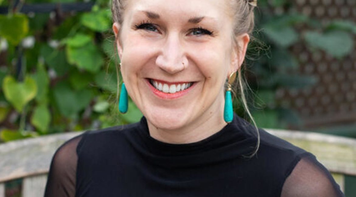 A smiling woman wearing a black top and turquoise earrings.