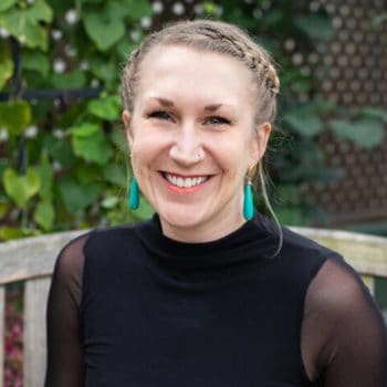 A smiling woman wearing a black top and turquoise earrings.