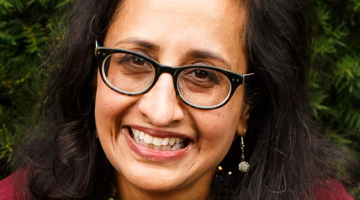 A woman wearing glasses and a maroon sweater smiles.