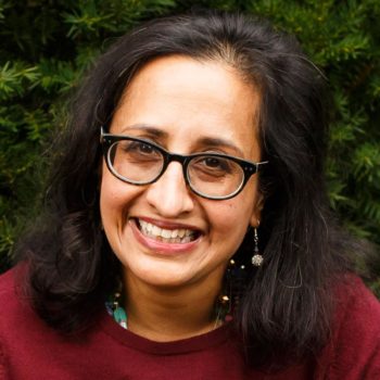 A woman wearing glasses and a maroon sweater smiles.