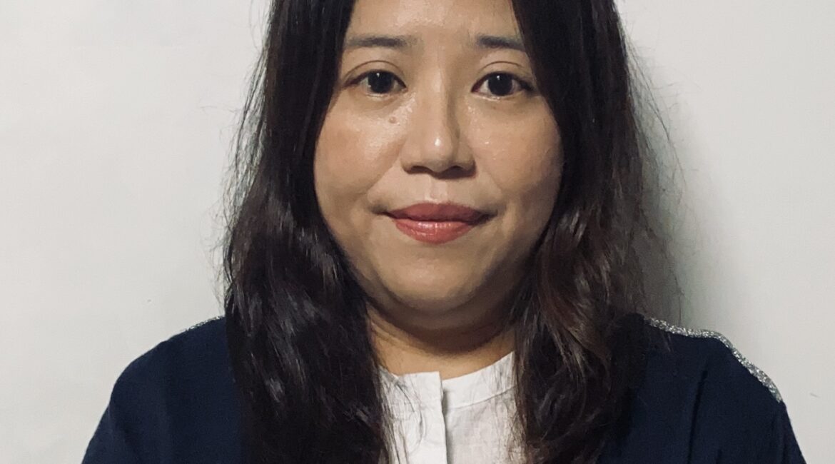 Trauma Solutions: A woman with long dark hair wearing a white shirt and dark cardigan stands against a plain light-colored background, looking at the camera.