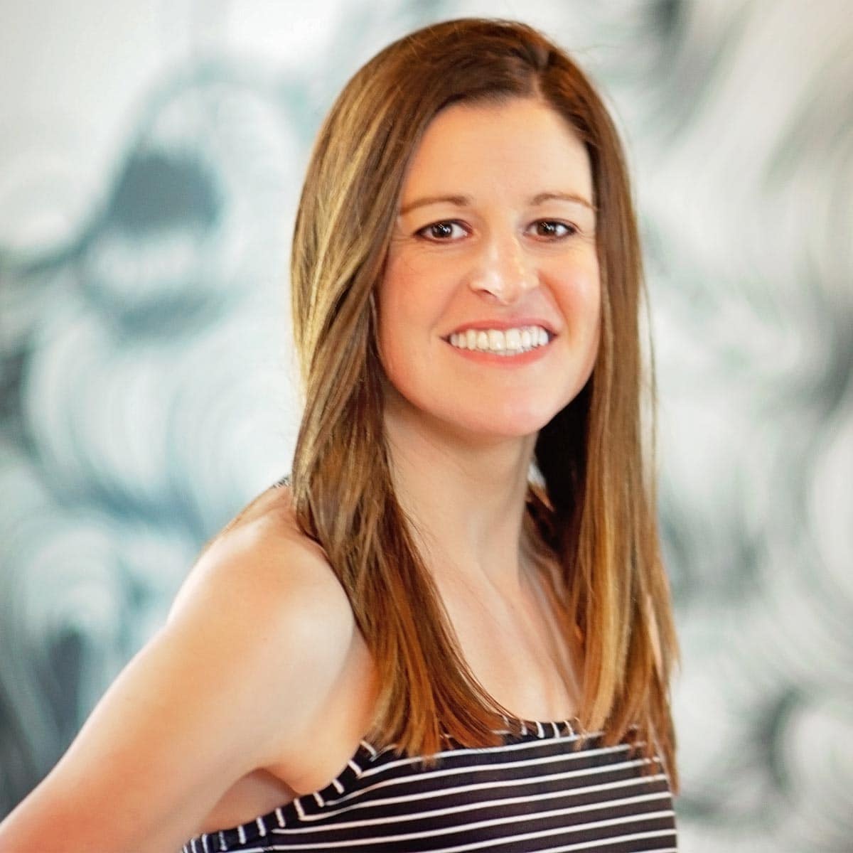 A woman in a striped top smiles in front of a wall.