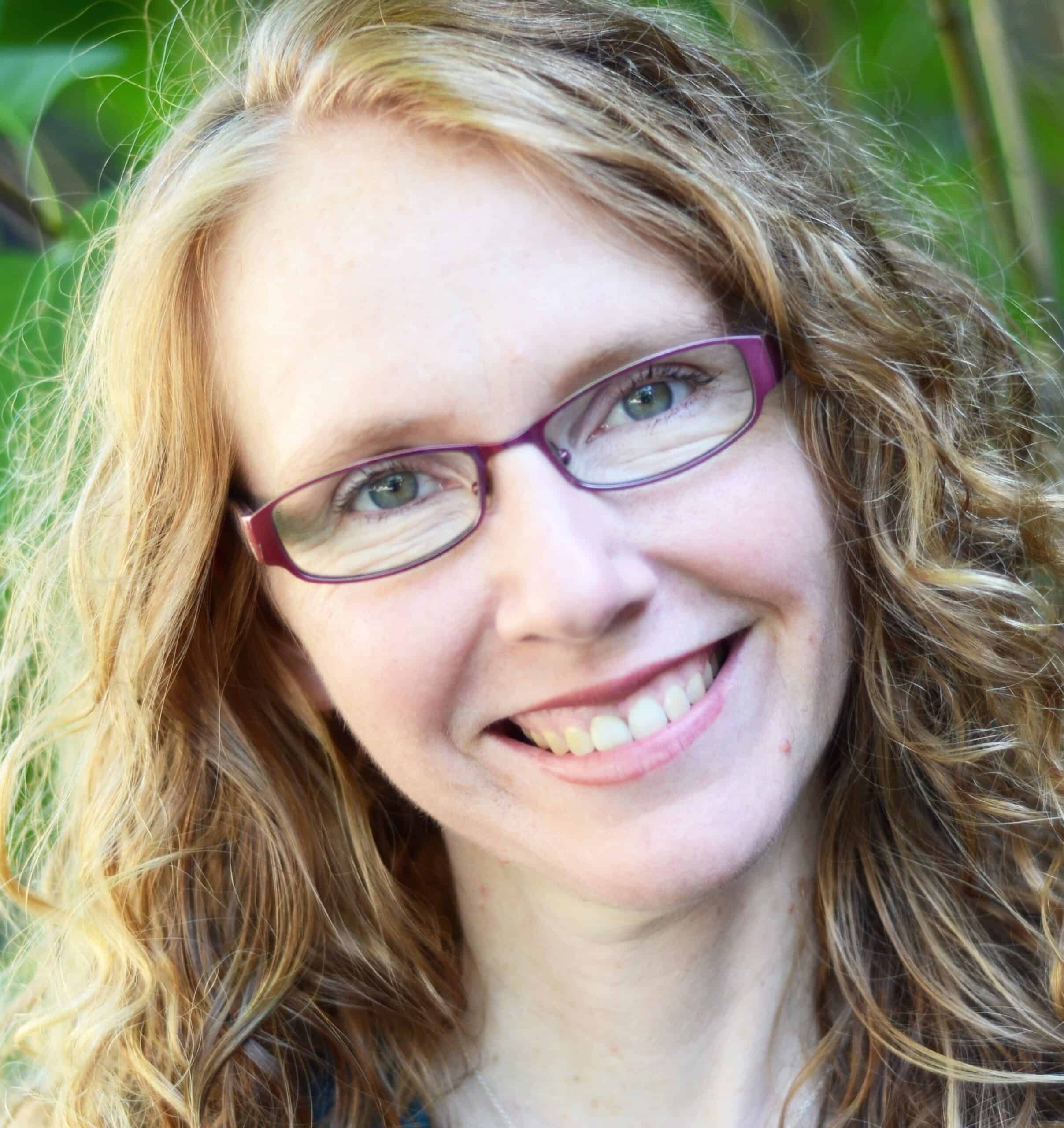 A woman with curly hair and glasses smiles for the camera.