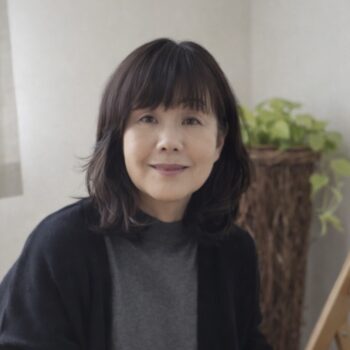 Trauma Solutions: A woman with shoulder-length dark hair and a grey top sits indoors, smiling softly. There is a green potted plant in the background.