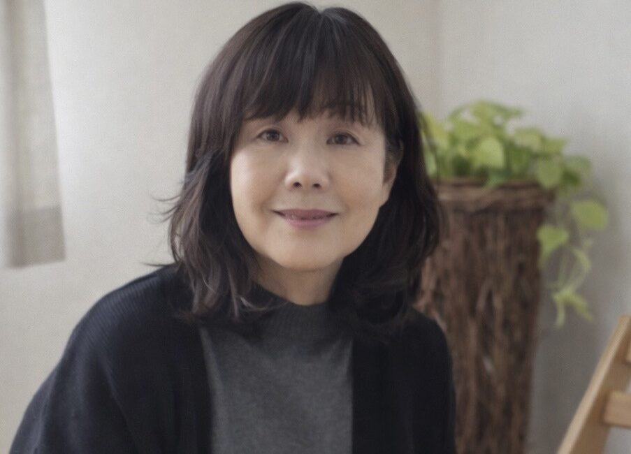 Trauma Solutions: A woman with shoulder-length dark hair and a grey top sits indoors, smiling softly. There is a green potted plant in the background.