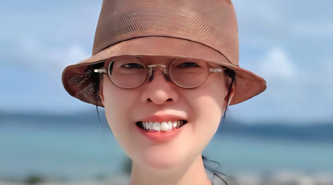 Solutions contre les traumatismes&nbsp;: Une personne portant un chapeau bob marron et des lunettes, souriant devant un arrière-plan océanique flou.