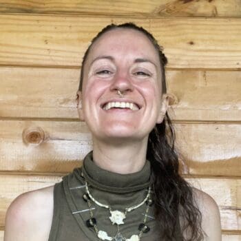 Trauma Solutions: A person wearing a sleeveless top and layered necklaces smiles in front of a wooden wall.
