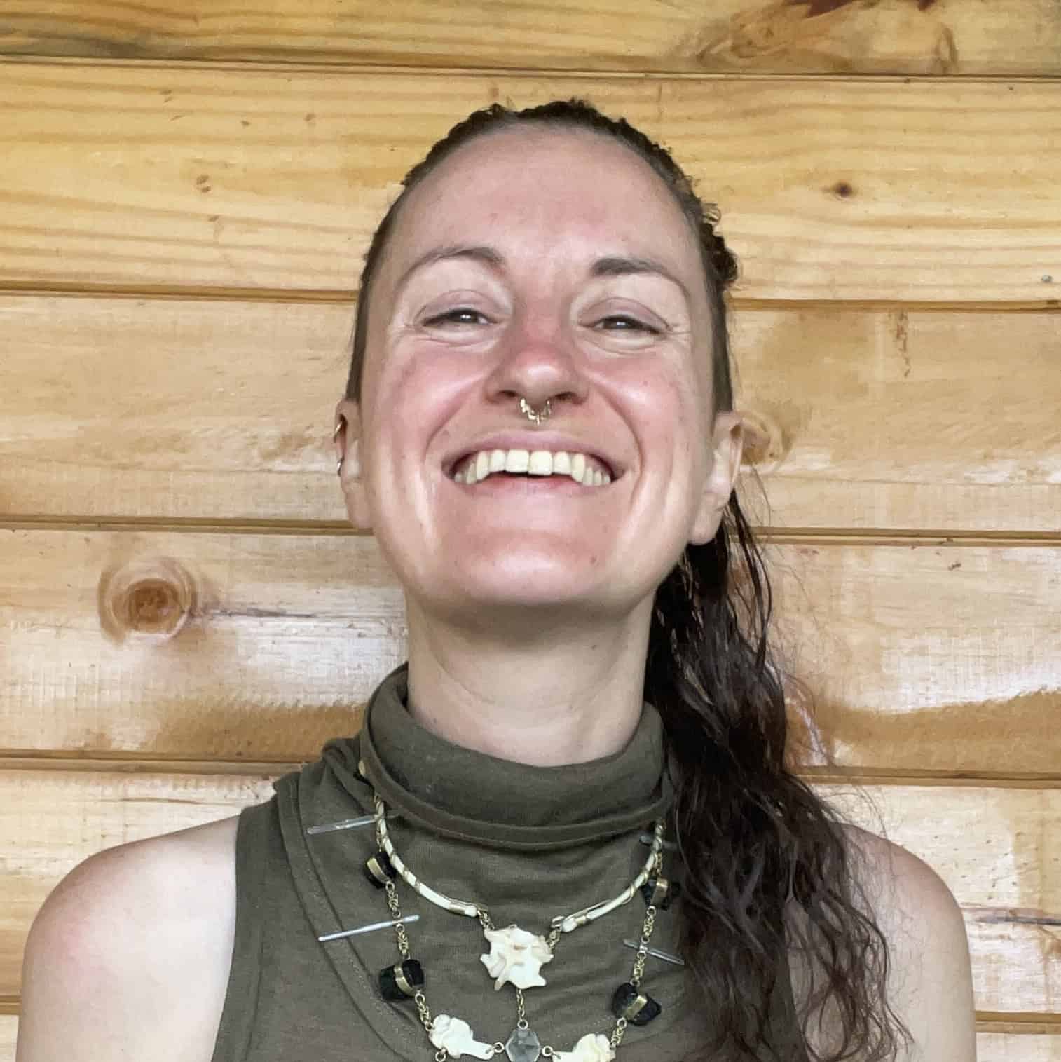 Trauma Solutions: A person wearing a sleeveless top and layered necklaces smiles in front of a wooden wall.
