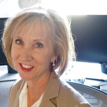 A woman in a tan suit smiling in front of a computer.