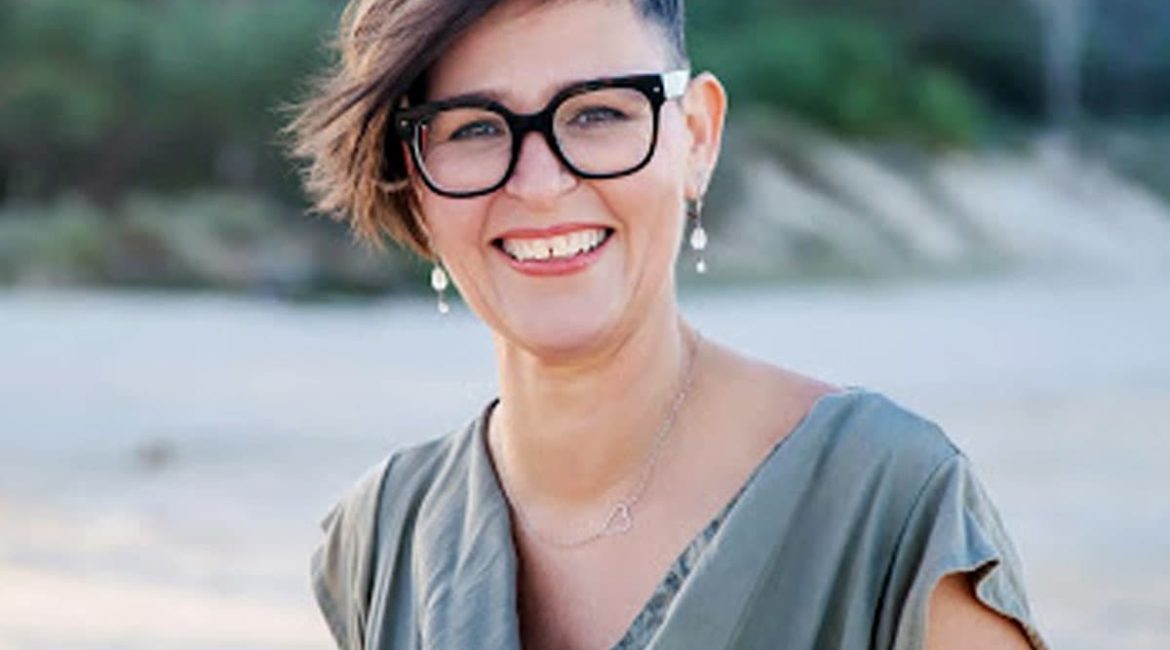 A woman wearing glasses and a green top standing on a beach.