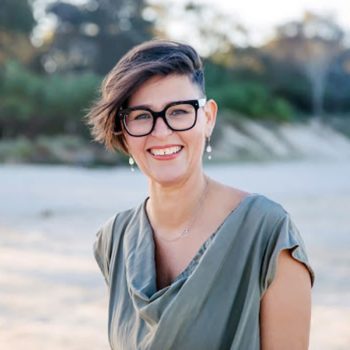 A woman wearing glasses and a green top standing on a beach.