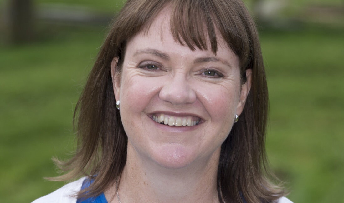 A smiling woman in a blue shirt standing in a field.