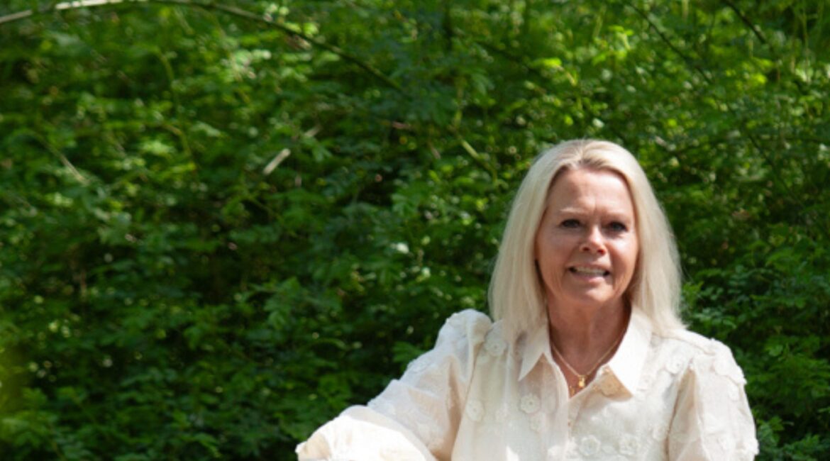 Solutions pour les traumatismes : Une femme aux cheveux blonds mi-longs est assise sur une bûche dans un jardin, vêtue d'un chemisier blanc et d'un jean bleu.