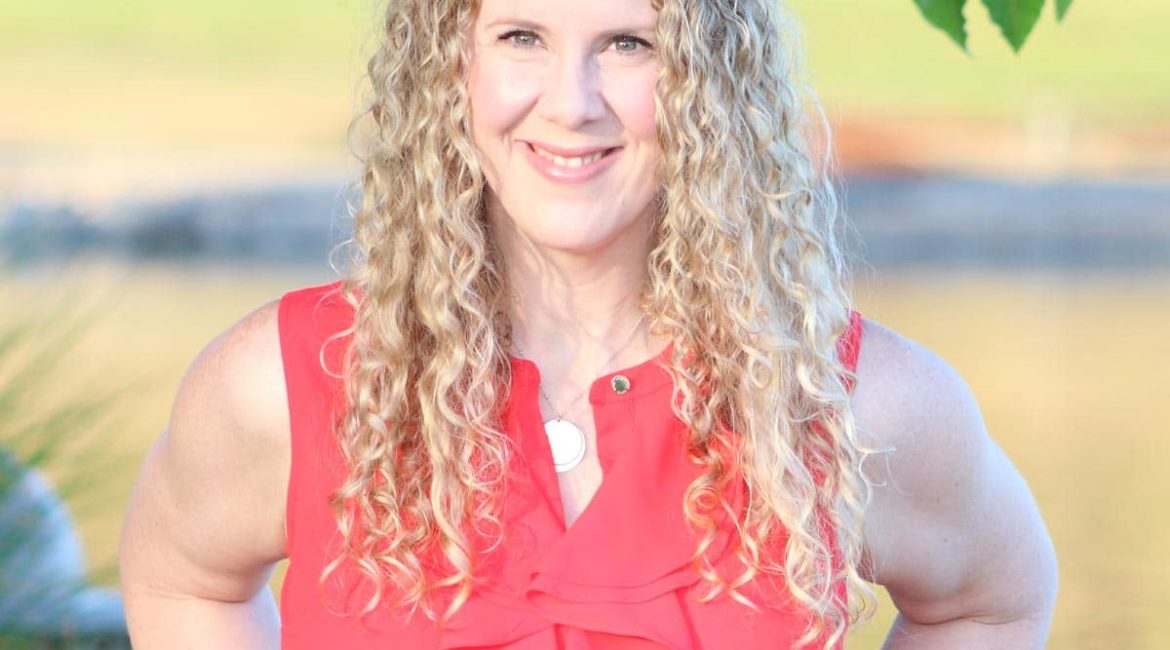 A woman with curly hair standing in front of a lake.