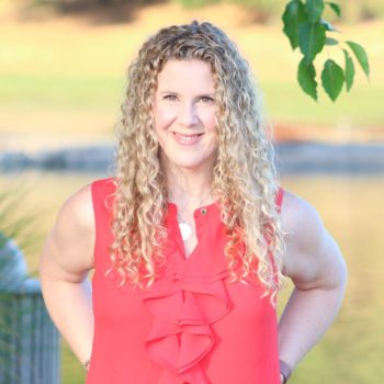 A woman with curly hair standing in front of a lake.