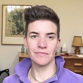 A man in a purple shirt is standing in front of a desk.