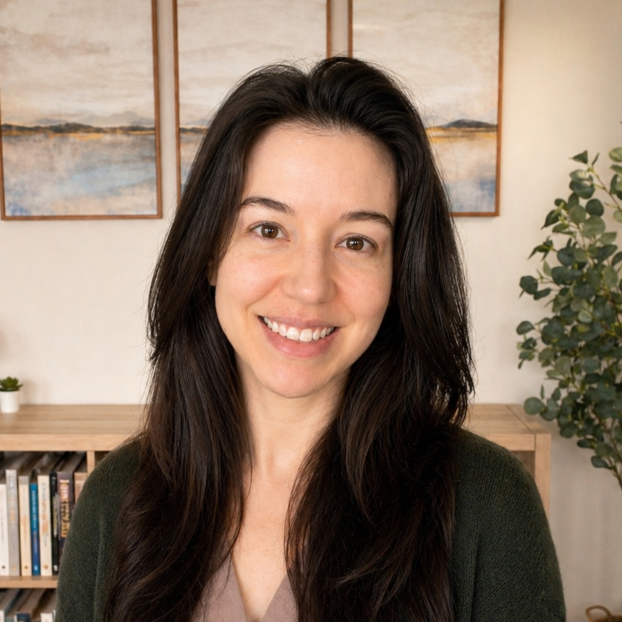 Trauma Solutions: A woman with long dark hair smiles at the camera, standing indoors with bookshelves, framed artwork, and a plant in the background.