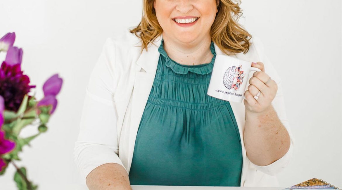 A woman sitting at a desk holding a coffee mug.