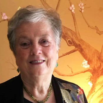 An older woman smiling in front of a wall.